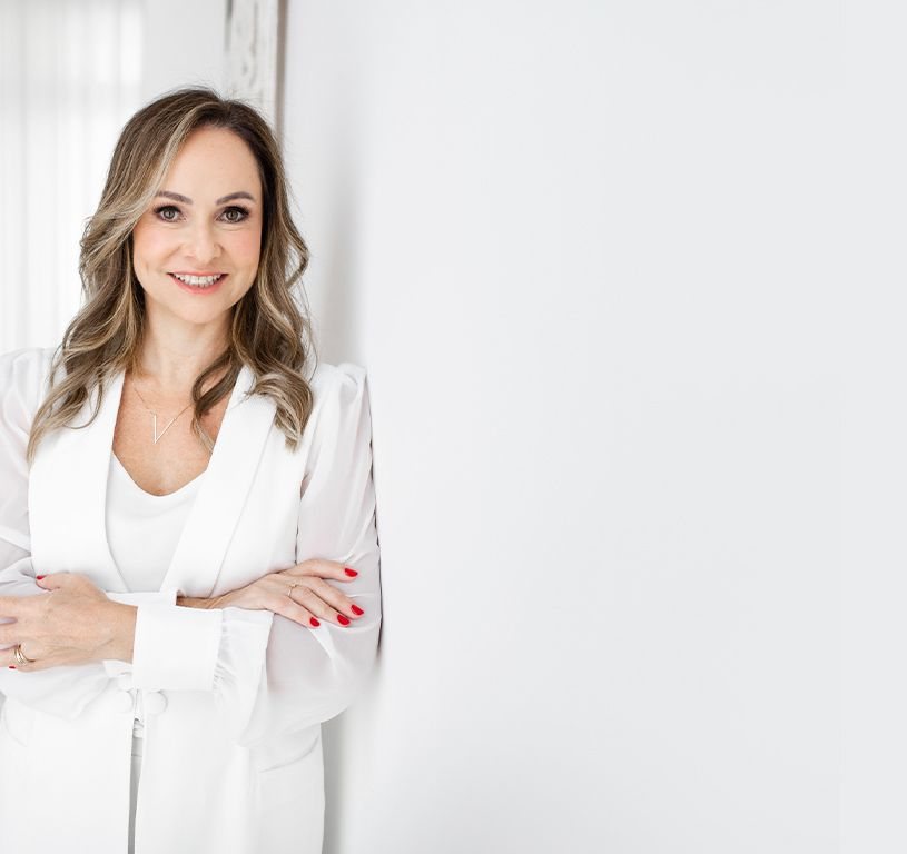 Dra. Alessandra Nalin em pé, de blazer branco, em ambiente claro